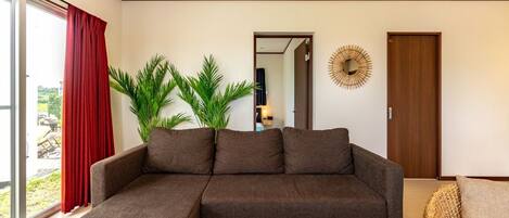 A modern living room with a sectional sofa, a wicker armchair, and a glass coffee table with two wine glasses.