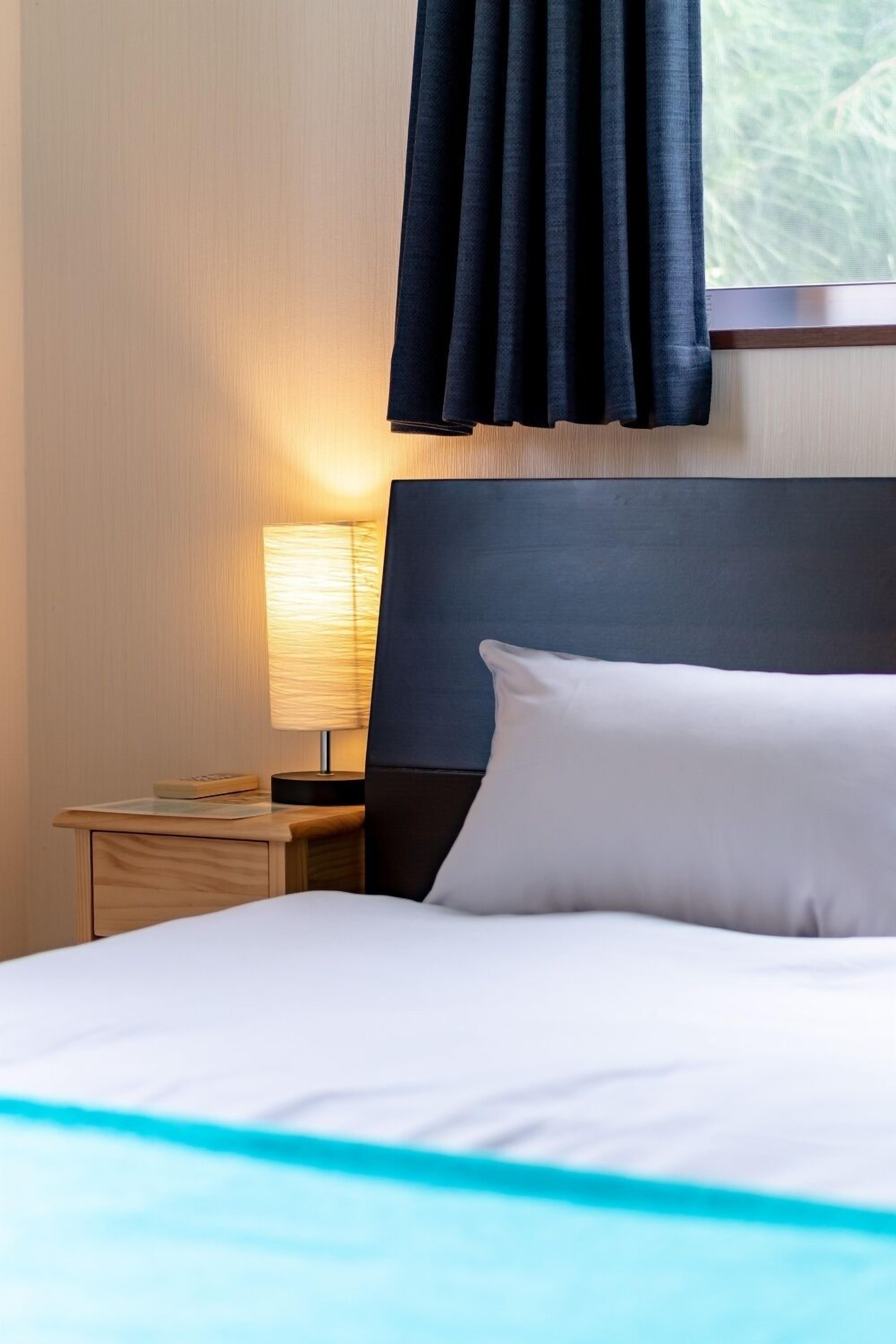 A neatly made bed with white bedding and a blue accent, a bedside lamp, and a dark headboard.