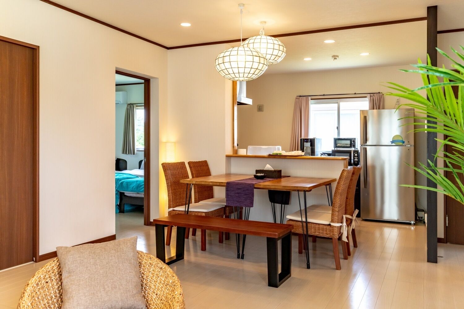 A modern hotel room with a dining area, a kitchenette, and a bathroom visible through an open door.