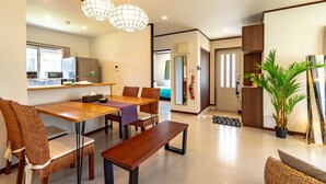 A modern living room with a wooden dining table, wicker chairs, a bench, and a large potted plant. - LiB PLUS Villa NAGO (Nago)
