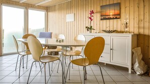 A dining area with a round table, six chairs, a white cabinet, and a painting of a sunset over water. - Cozy home in Hemmet with house sea view (Hemmet)