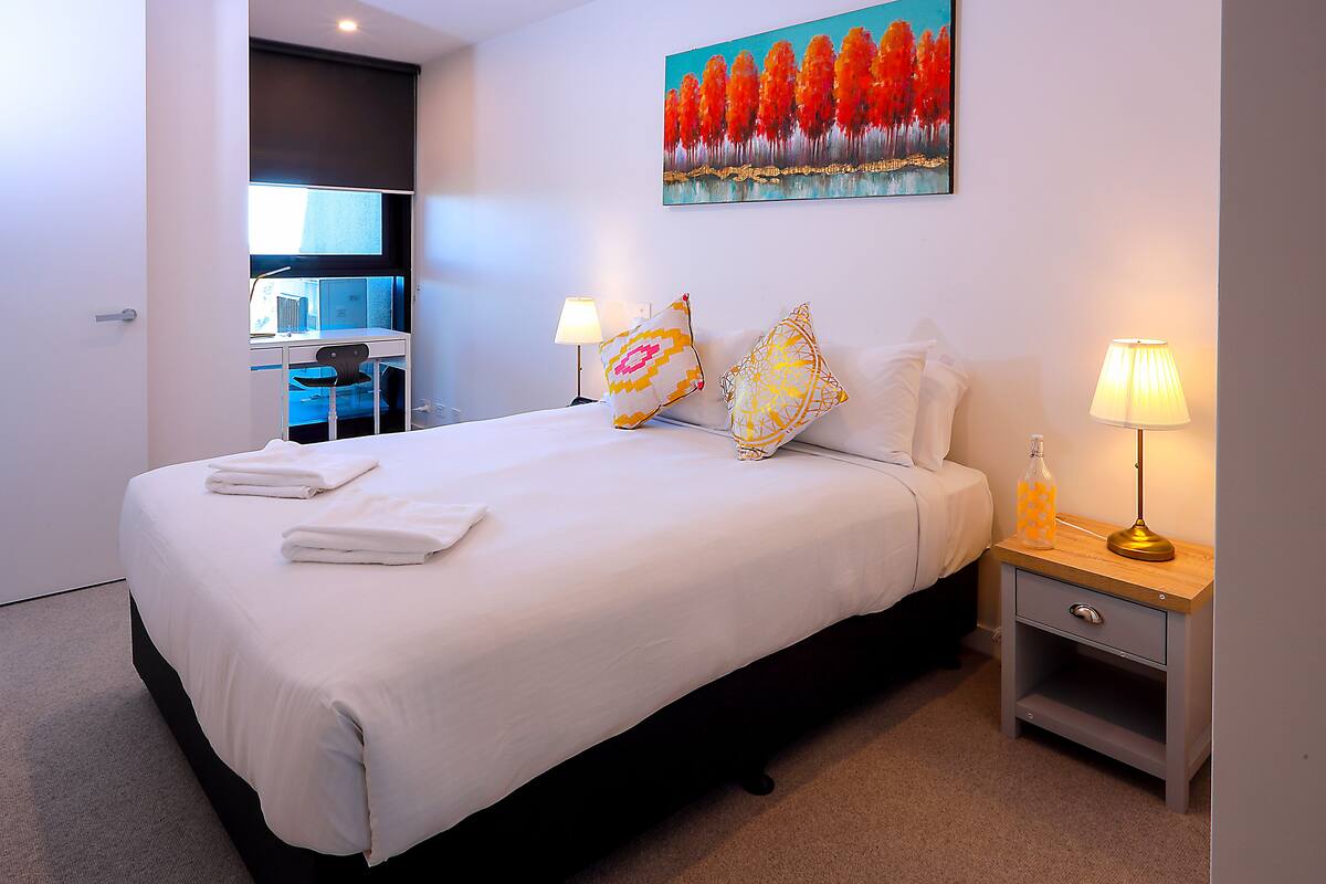 A neatly made bed with pillows and a bedside table with lamps.