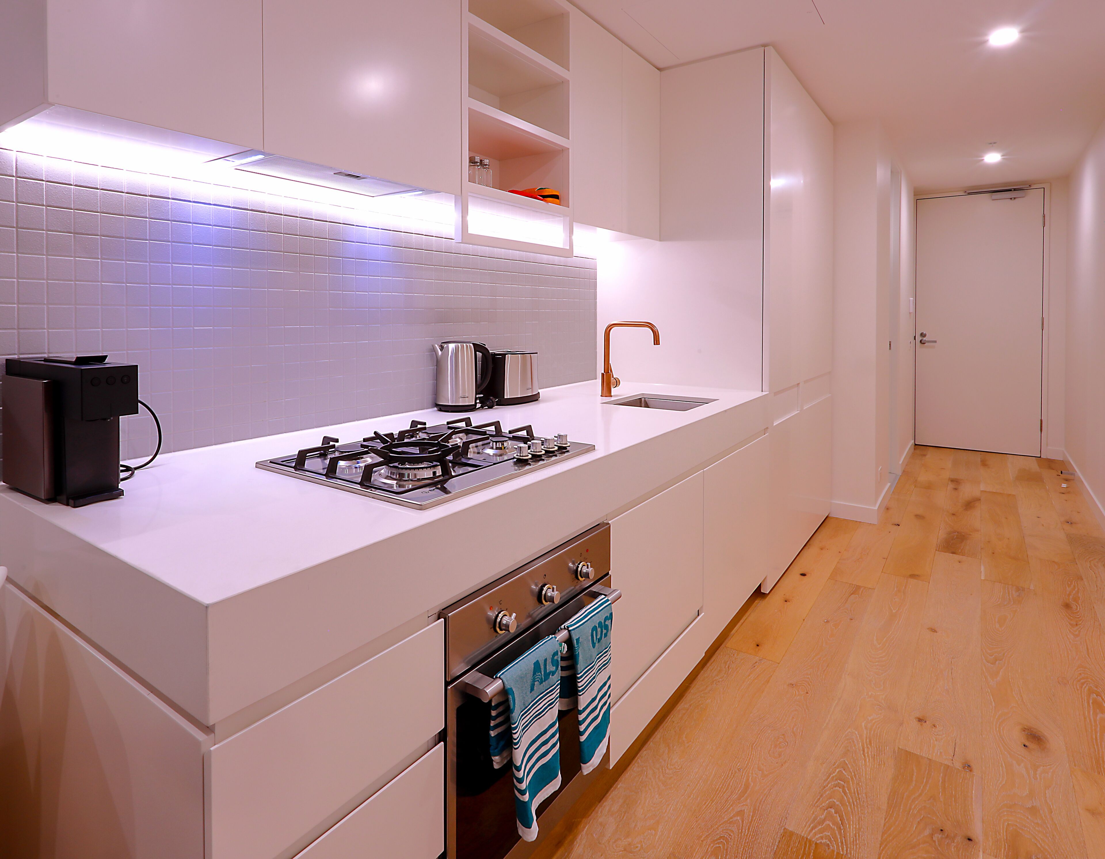 A modern kitchen with white cabinetry, a gas stove, a coffee machine, and a sink.