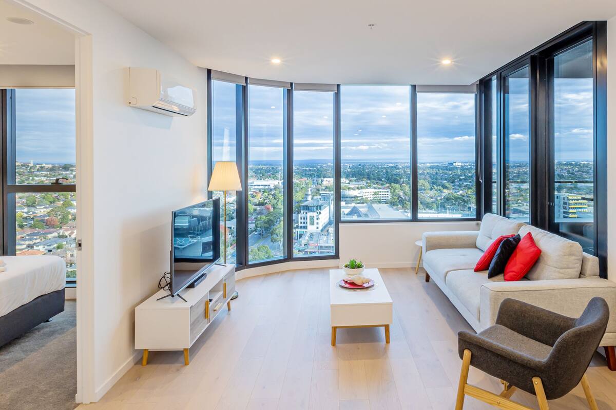 A modern living room with a large window, a sofa, a coffee table, and a TV.