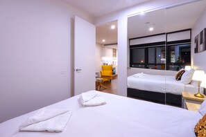 A hotel room with a large bed, a mirror, a yellow chair, and a nightstand with a lamp. - Astra Apartments Glen Waverley @ O'Sullivan RD (Glen Waverley)
