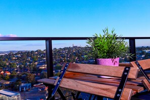 A balcony with wooden chairs and a potted plant, overlooking a residential area. - Astra Apartments Glen Waverley @ O'Sullivan RD (Glen Waverley)