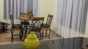 Et spiseområde med et rundt bord og fire stole, en loftsvifte og et vindue med lette gardiner.