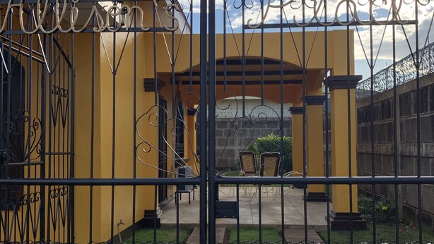 En hegnet indgang med en gul bygning og en pergola.