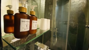 A bathroom with a glass shower enclosure, a glass shelf with toiletries, and a bathtub. - Guest House Conext (Kowloon)
