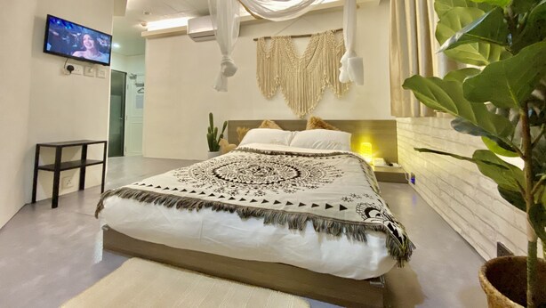 A modern bedroom with a large bed, a TV on the wall, and a plant. - Guest House Conext (Kowloon)