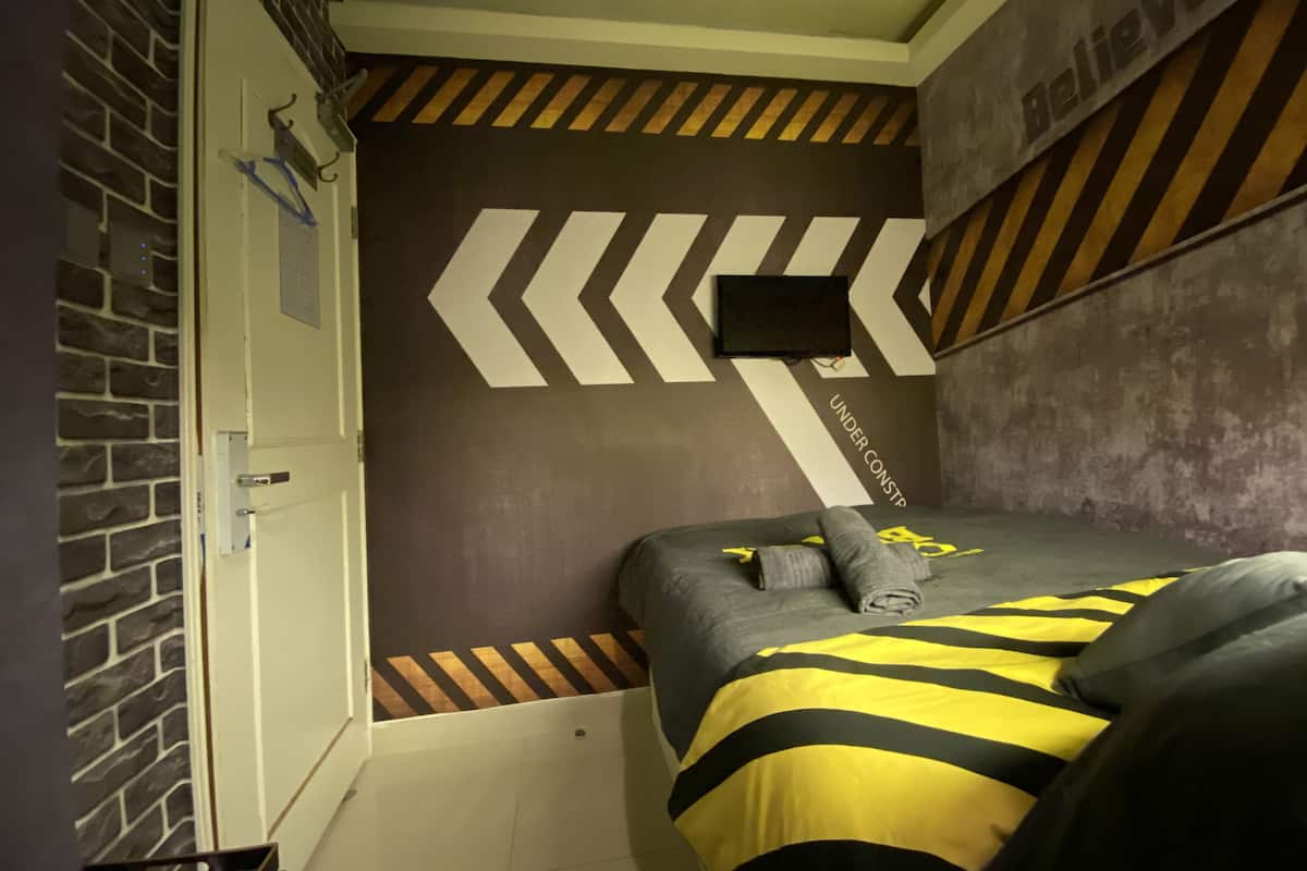 Une chambre à coucher avec un lit, un téléviseur fixé au mur et un mur décoré d’un motif en briques.