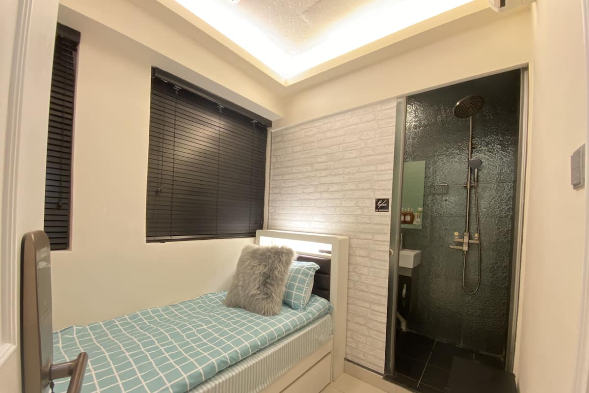 Une petite chambre comprenant un lit, une douche et une petite fenêtre avec des stores.