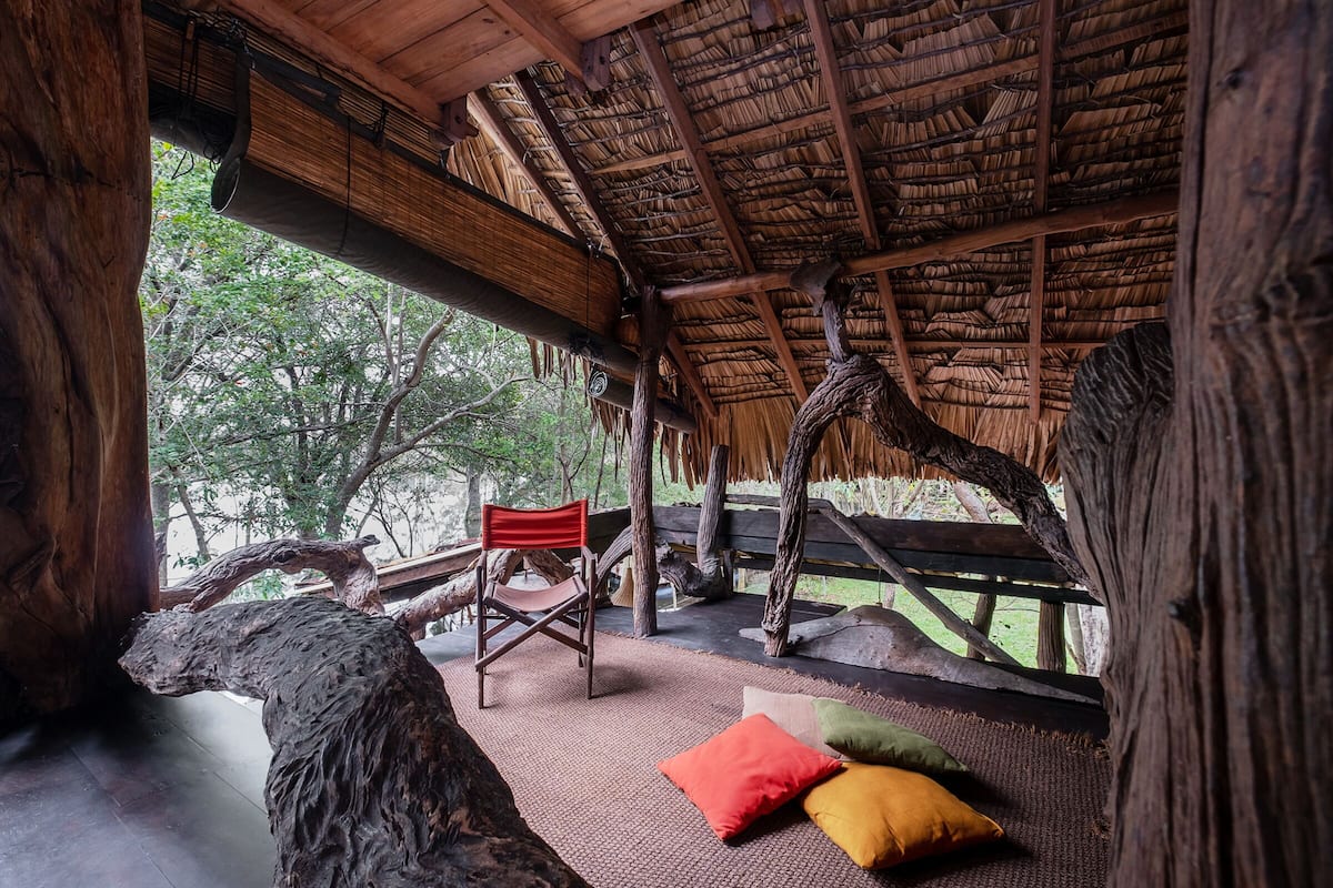 A rustic wooden structure with a thatched roof, a wooden chair, and a bench with cushions.