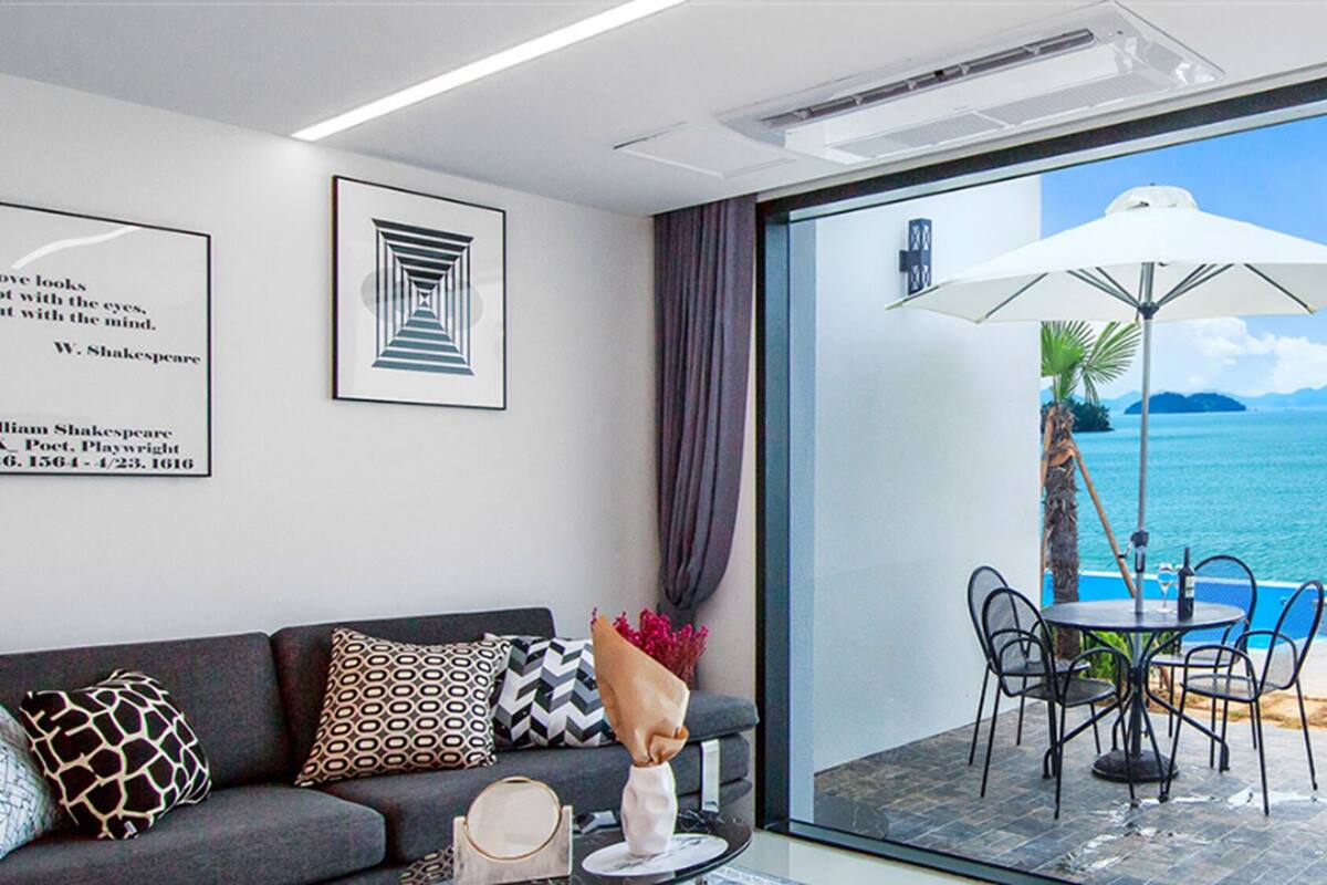 A modern room with a sofa, a table with chairs, and a view of the sea through large glass doors.
