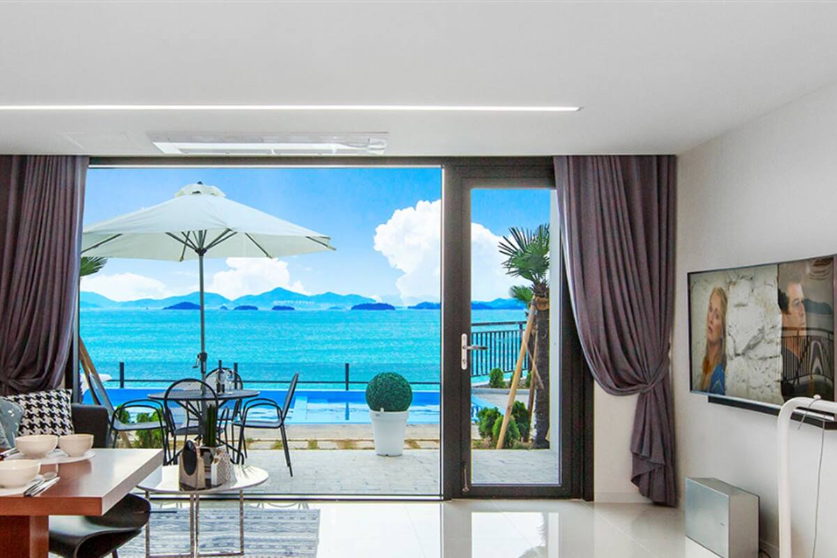 A modern room with a view of the sea, a dining area with a table and chairs, and a large window with curtains.