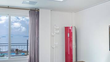 A room with a large window overlooking a body of water, a red air conditioning unit, and a framed photograph on the wall.