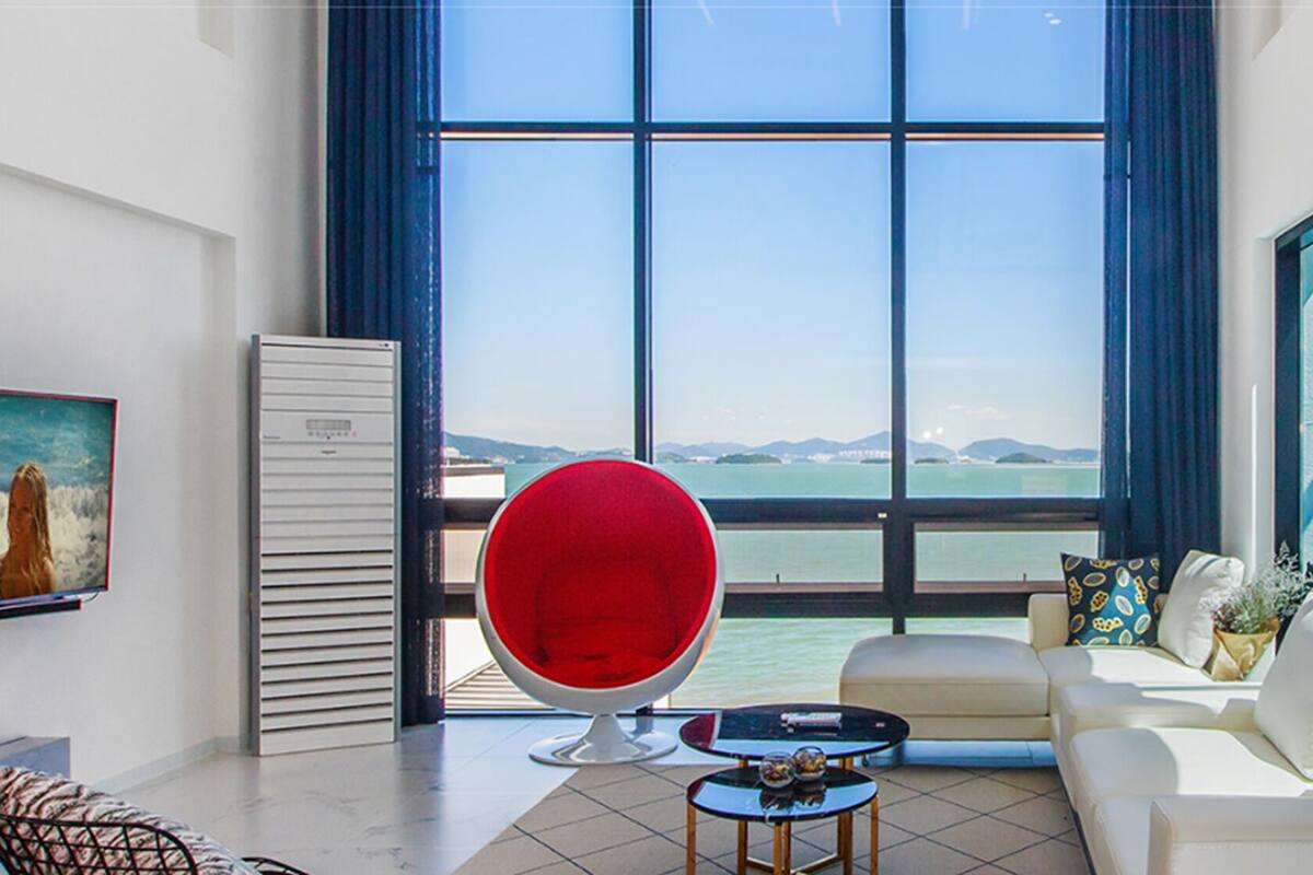 A modern living room with a large window, a red chair, a white sofa, and a small table.