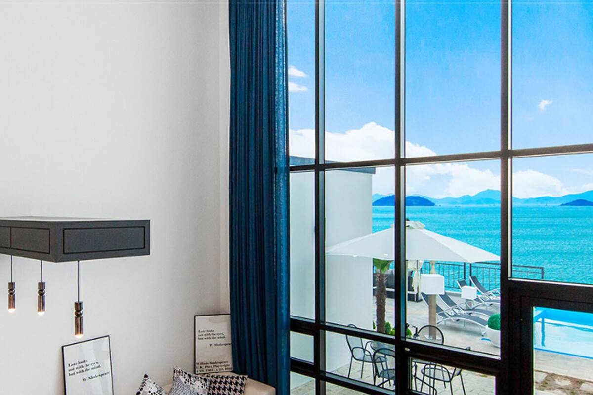 A hotel room with a large window offering a view of the sea and mountains.
