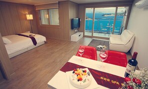 Habitación de hotel con cama, televisión, zona de comedor con mesa para dos y balcón con vista al mar.