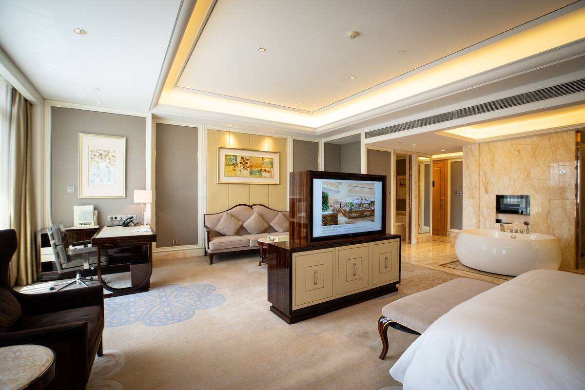 Ett modernt hotellrum med en stor säng, en soffa, ett skrivbord med en dator, en tv och ett badkar.