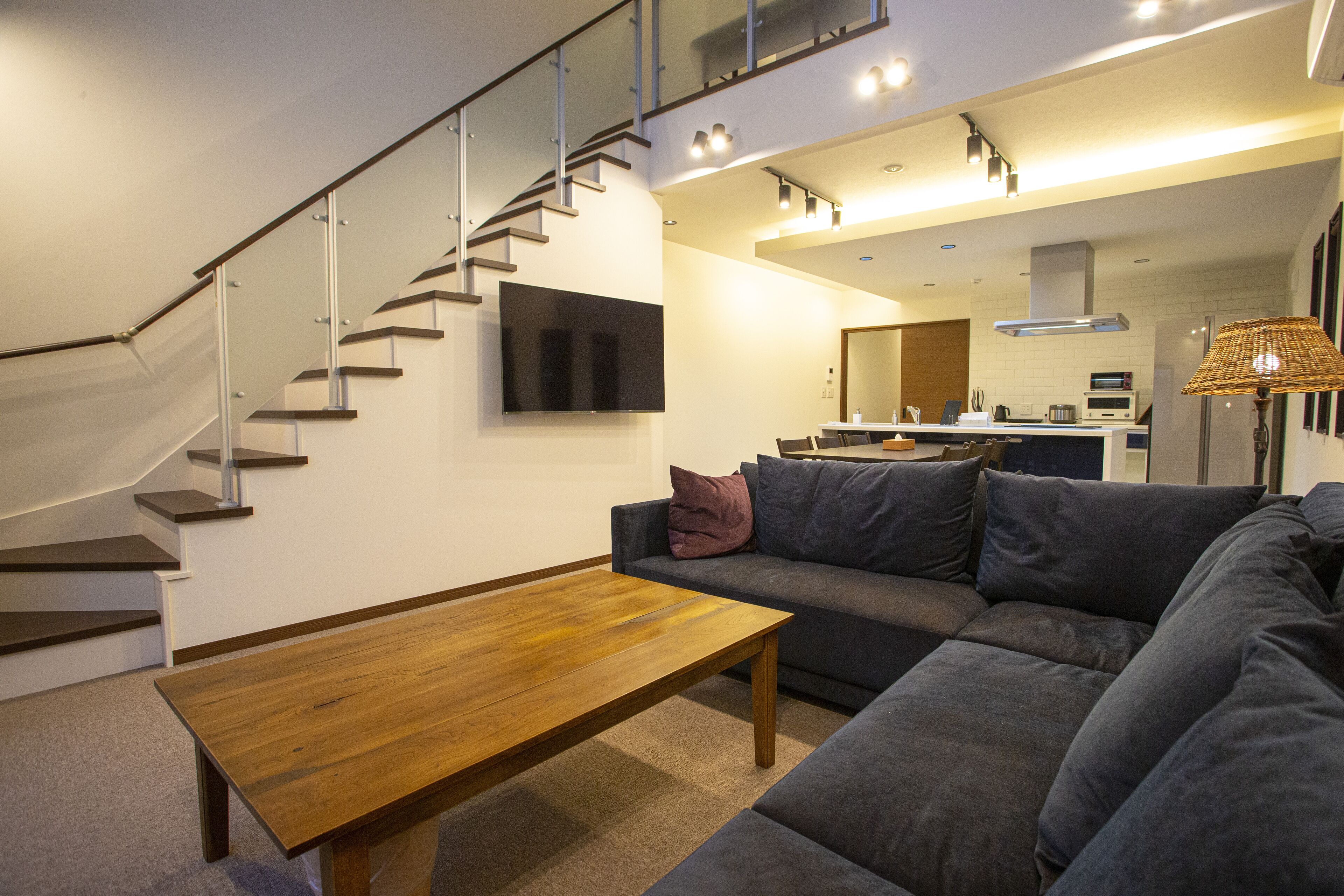 A modern living room with a wooden coffee table, grey sofa, and a staircase leading to an upper level.
