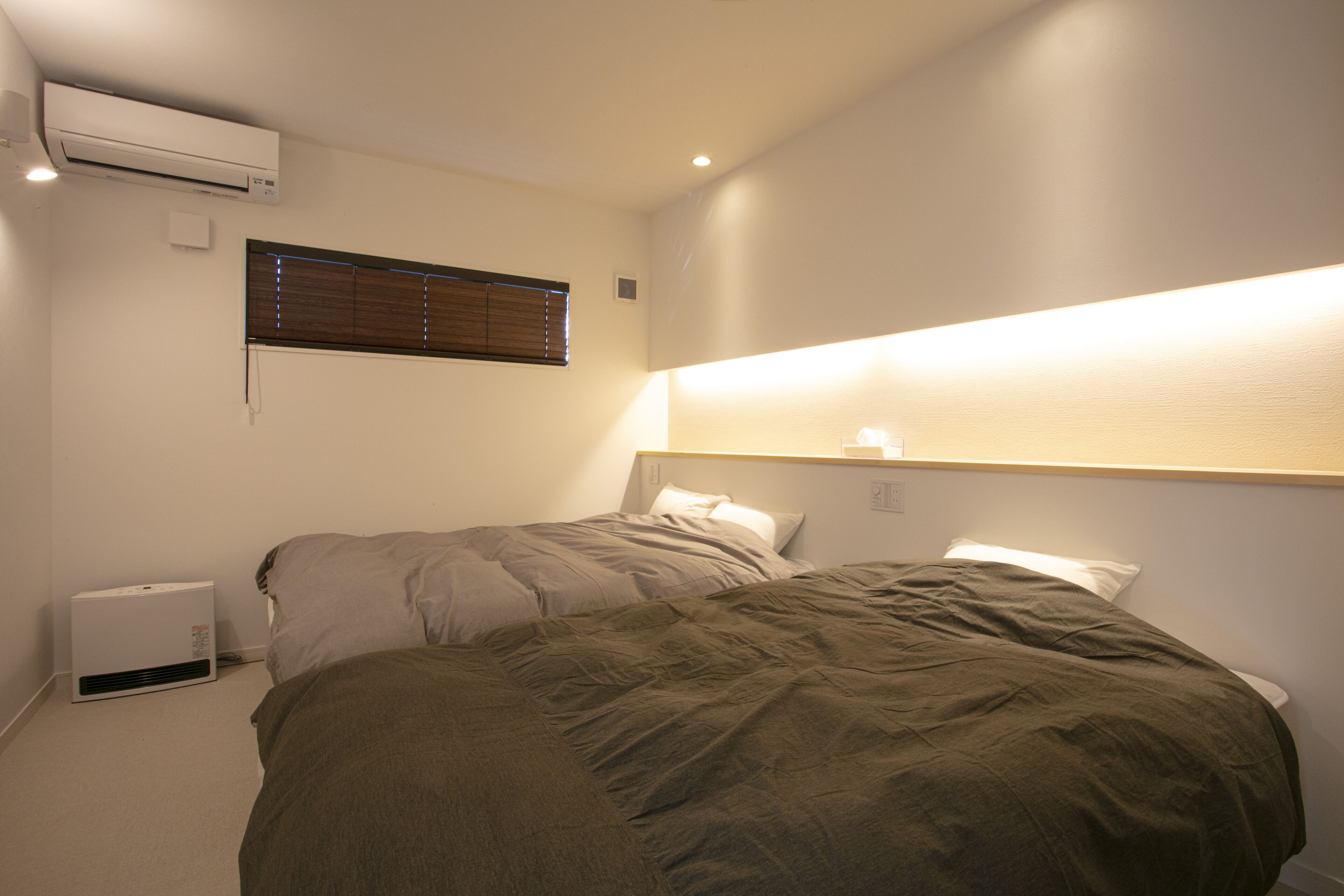 A bedroom with two beds, an air conditioner, a window with blinds, and a wall-mounted light fixture.