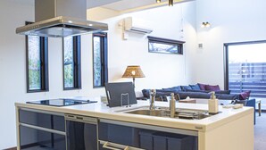 A modern kitchen with a central island, built-in appliances, and a seating area with a sofa and lamp. - Setsu (Fujikawaguchiko)