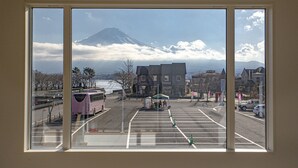 A view through a window of a parking lot with a bus, tents, and buildings in the background. - Setsu (Fujikawaguchiko)