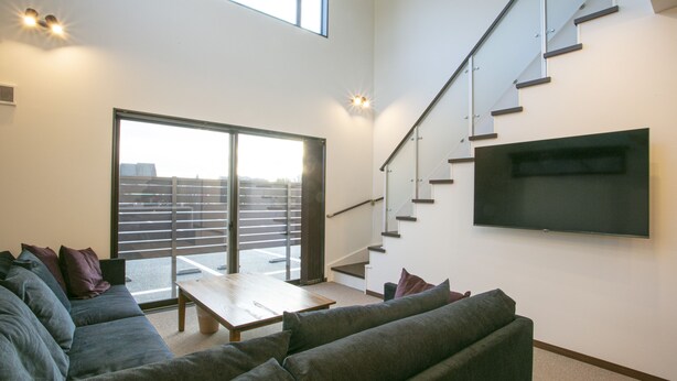 A spacious living area with a large window, a staircase, and a flat-screen TV mounted on the wall. - Setsu (Fujikawaguchiko)