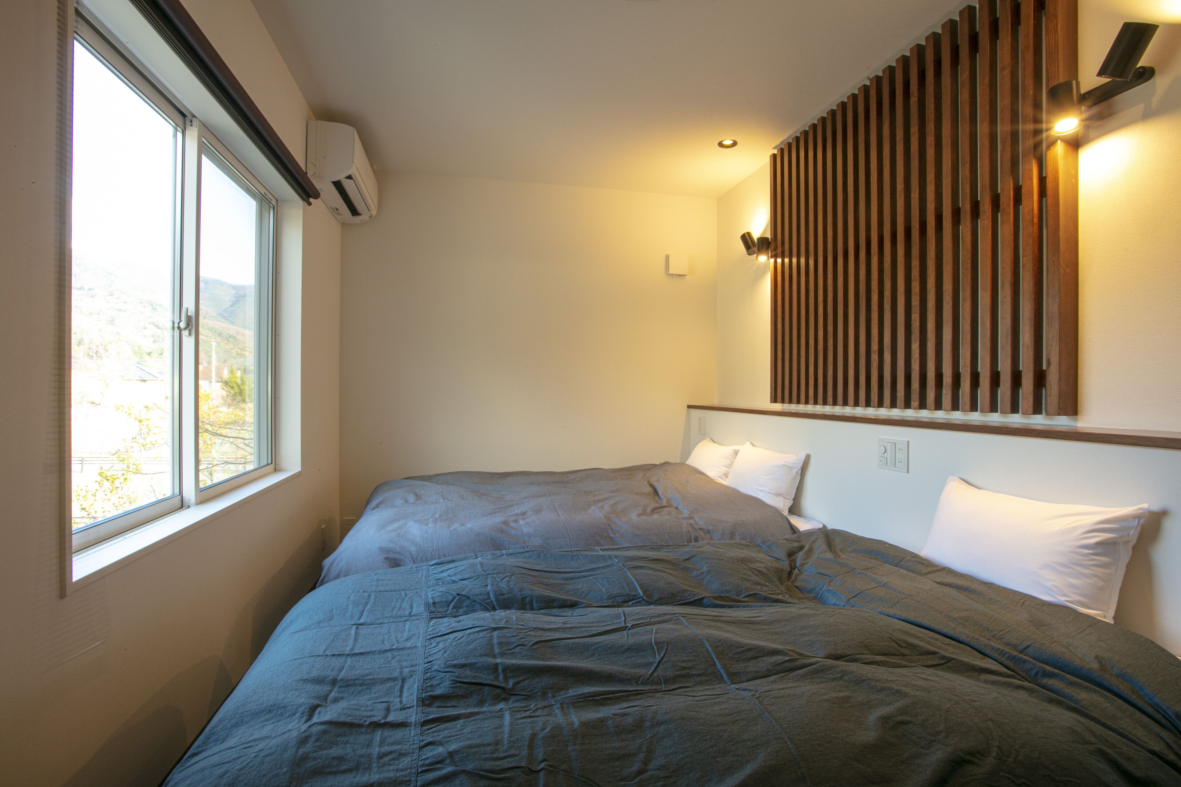 A bedroom with a large bed, a window, and a wall-mounted light fixture.