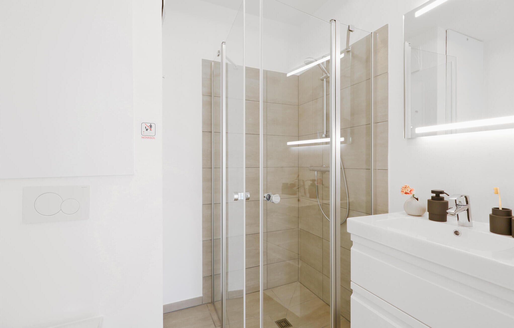 A modern bathroom with a glass-enclosed shower, white vanity, and a mirror above the sink.