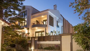 A modern two-story house with a balcony, stone wall, and potted plants.