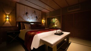 A traditional Japanese-style bedroom with a bed, bedside lamps, a nightstand, a bench, and a decorative wall piece. - Tenyu (Kyoto)