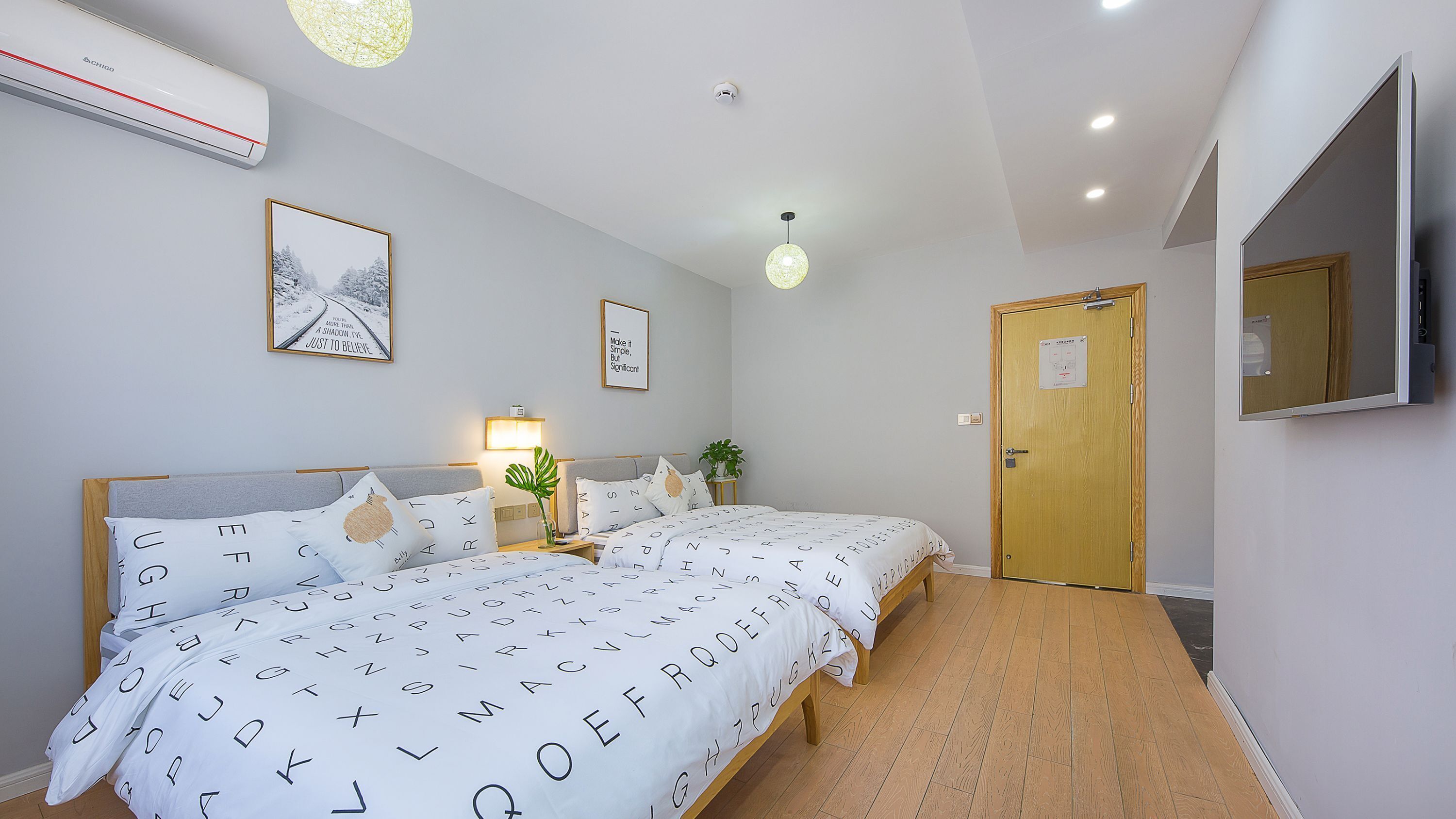 A bedroom with a bed, bedside tables, a wall-mounted air conditioner, a ceiling light, and a door with a mirror.