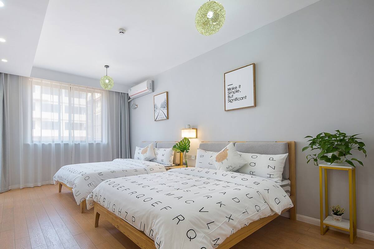 Un dormitorio moderno con dos camas, un ventanal con cortinas, una lámpara en el techo y una cita enmarcada en la pared.