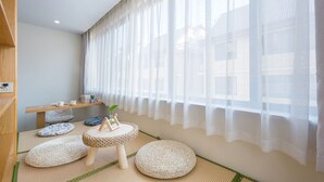 Una habitación con esteras de tatami, una mesa de madera baja con libros y una planta, y un ventanal con cortinas translúcidas.
