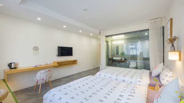 Une chambre d’hôtel moderne équipée d’un lit, d’un bureau, d’une chaise, d’une télévision et d’une salle de bain visible à travers une porte en verre.