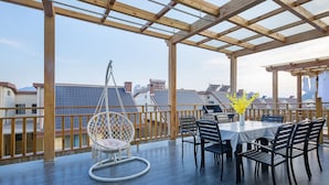 Una terraza en la azotea con una pérgola de madera, un sillón colgante, una mesa con sillas y un florero con flores.
