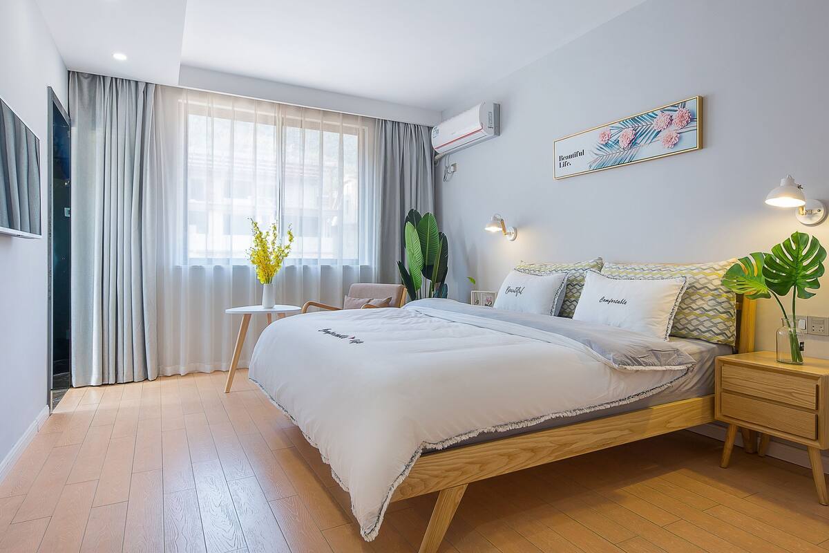 Un dormitorio moderno con cama de madera, una mesita de noche, una ventana con cortinas, aire acondicionado de pared y un cuadro enmarcado.