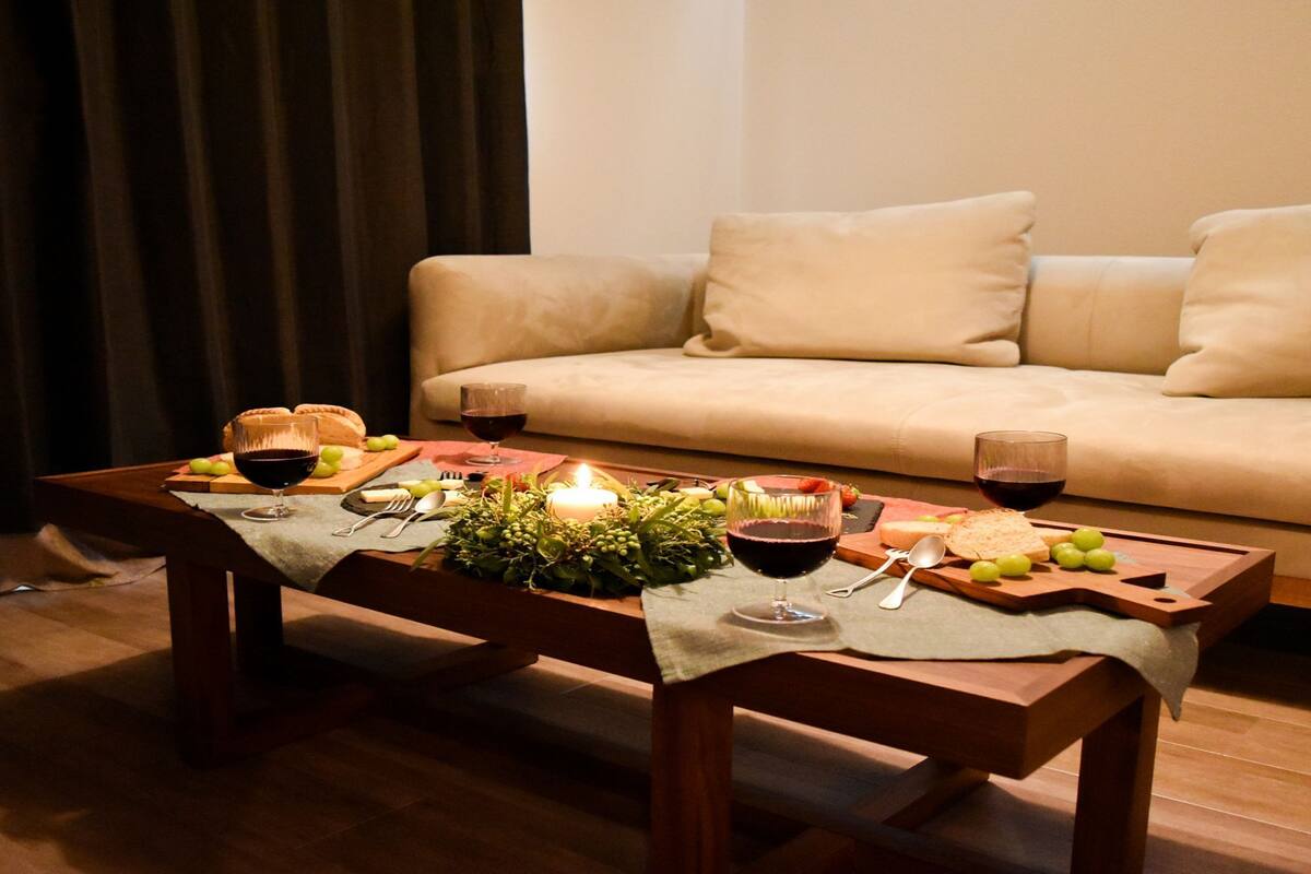 A cozy living room with a wooden coffee table set for a meal, a sofa, and a lit candle.
