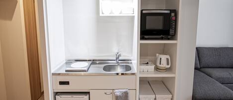 Uma cozinha compacta equipada com micro-ondas, pia e pequeno frigorífico.