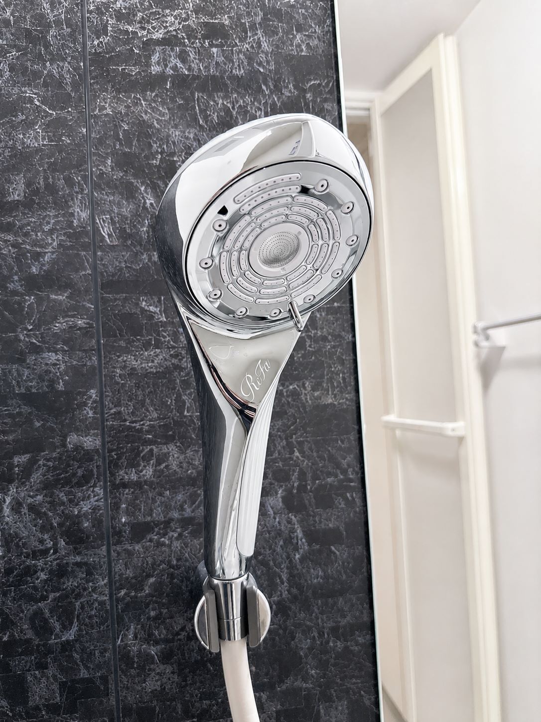 A chrome showerhead mounted on a wall with a marble-like texture.