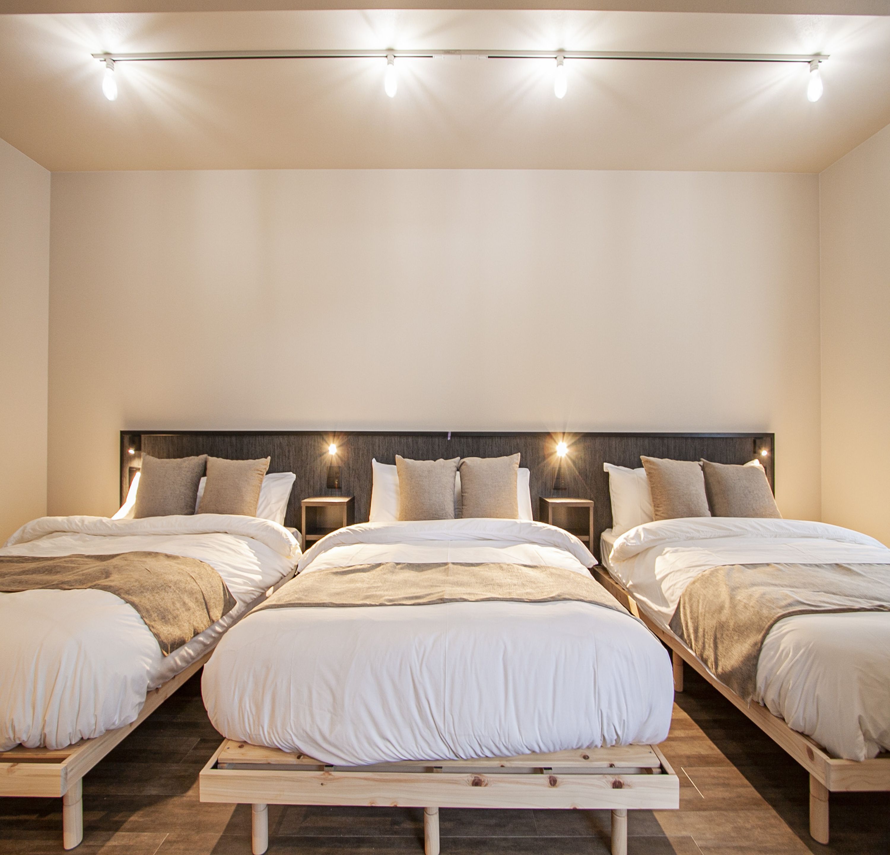 A modern bedroom with three beds, a wooden headboard, and bedside lamps.