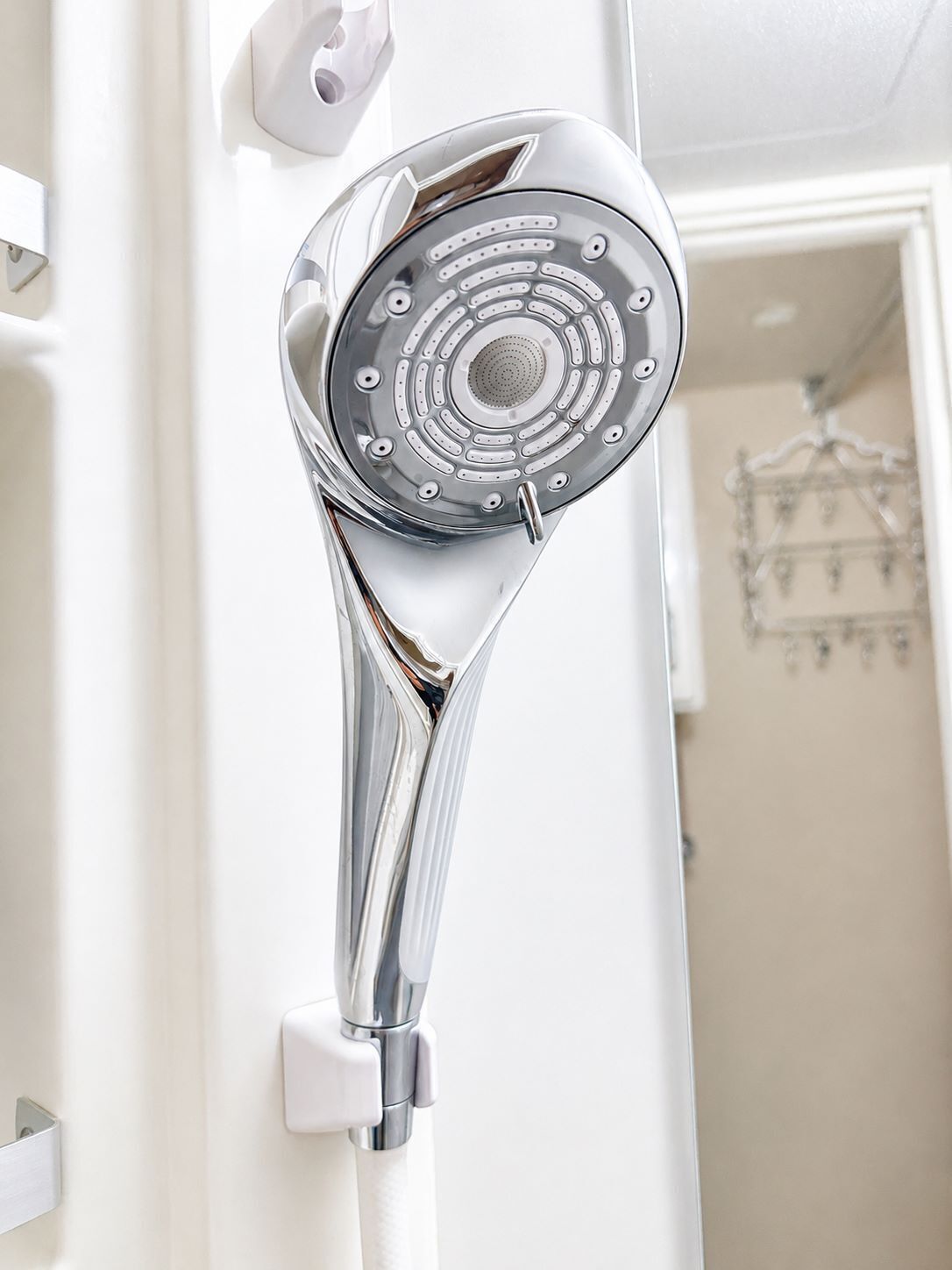 A modern showerhead with a chrome finish, mounted on a white wall.