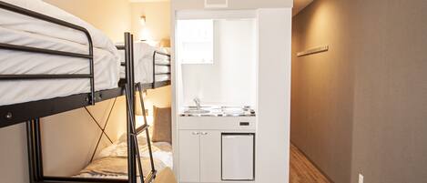 Una habitación pequeña con literas, kitchenette y un rincón de descanso.