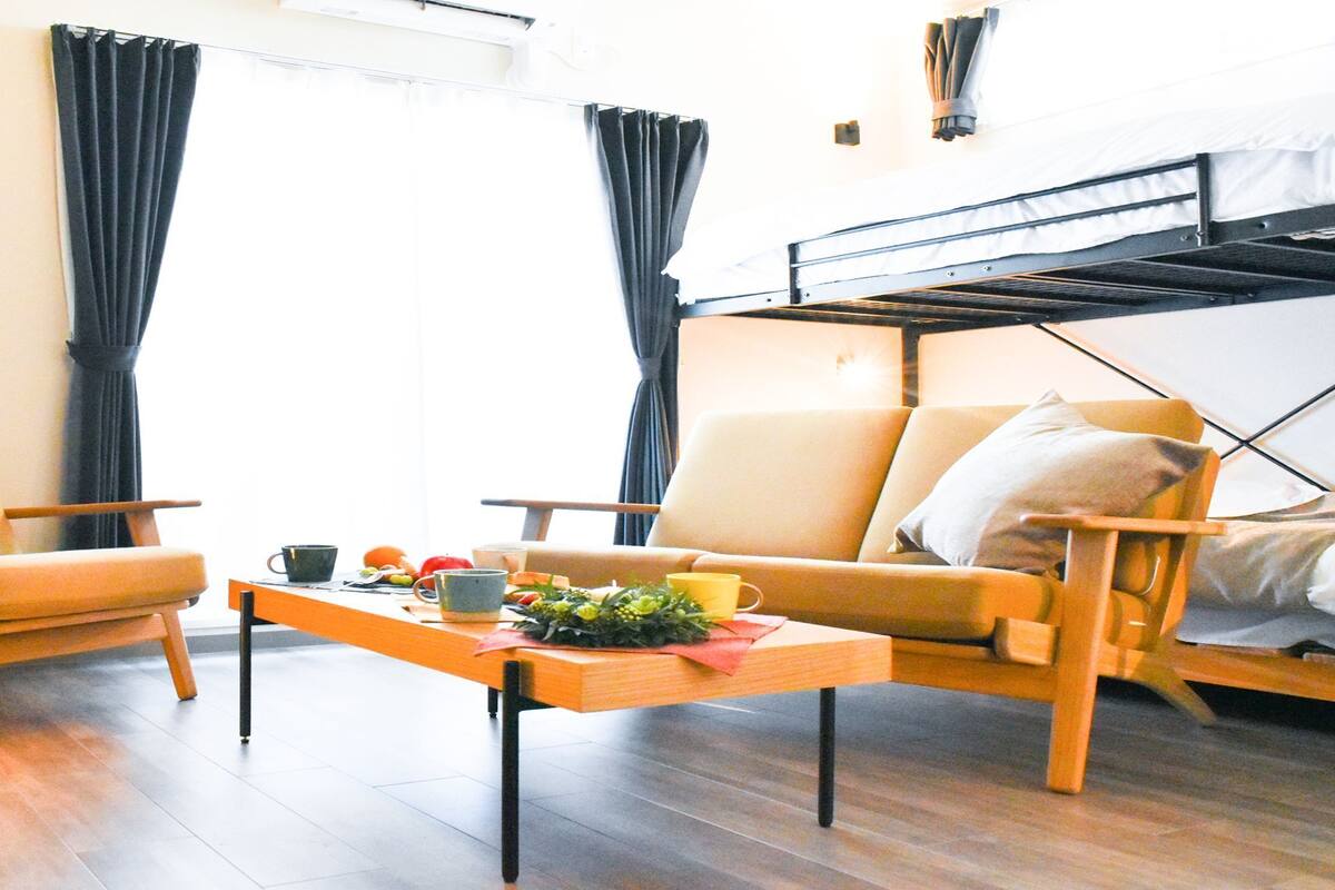 A compact living space with a sofa, two armchairs, a small table, and a bunk bed.
