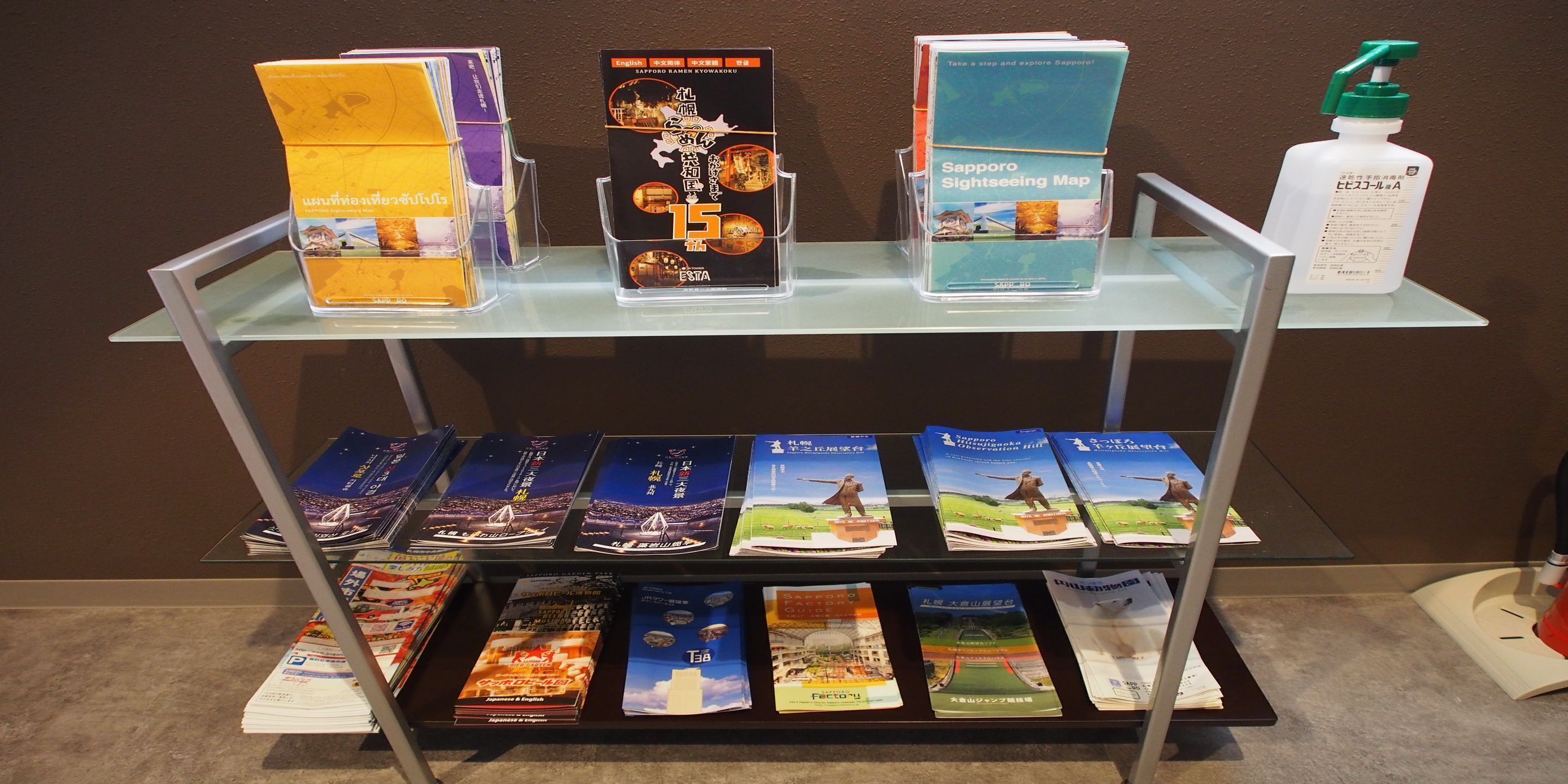 A display of travel brochures and a bottle of hand sanitizer on a glass shelf.
