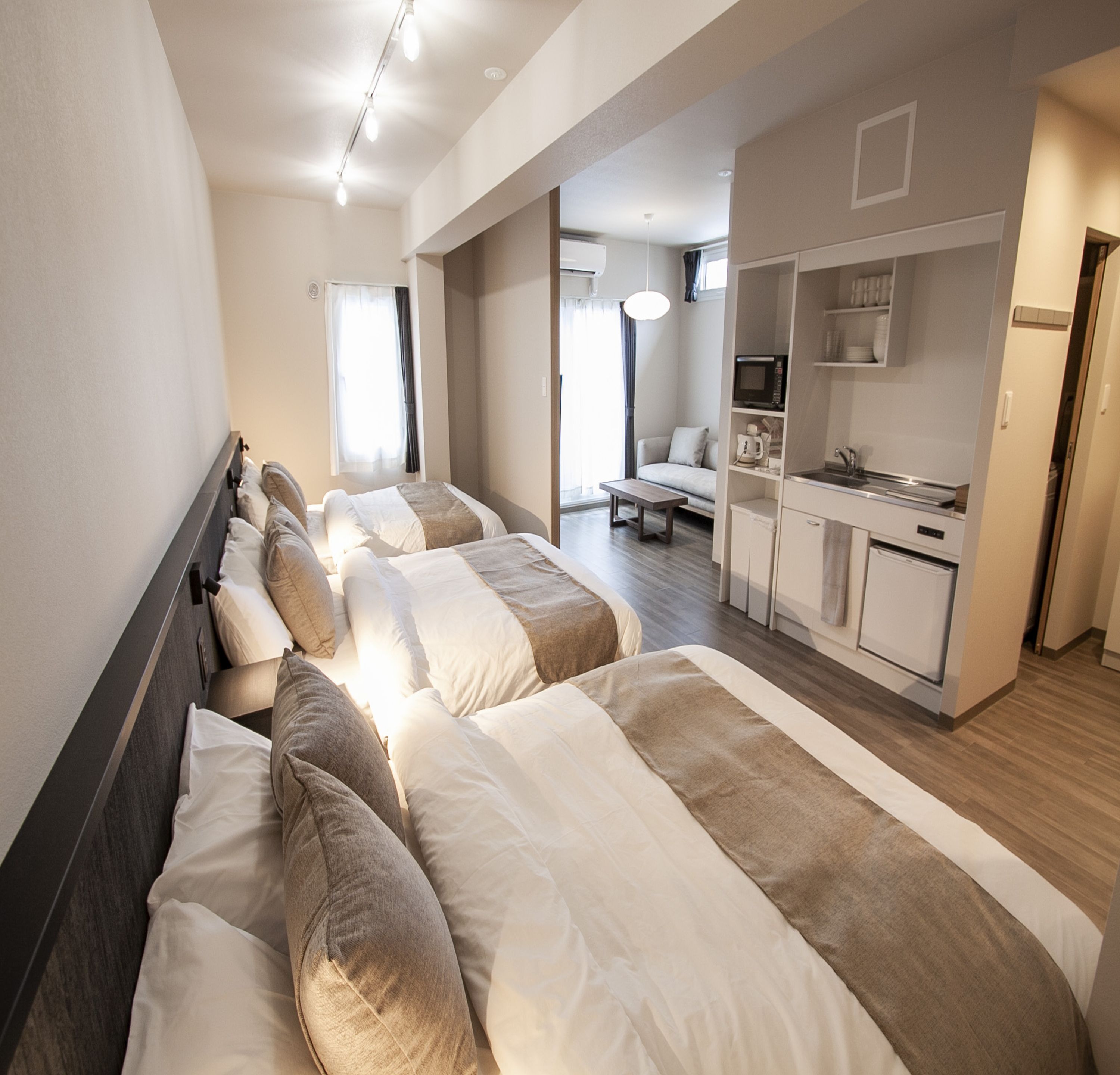 A hotel room with three beds, a kitchenette, and a seating area with a sofa and table.