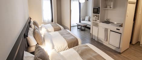 A hotel room with three beds, a kitchenette, and a seating area with a sofa and table.