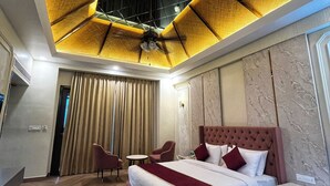 Ein Hotelzimmer mit einem großen Bett, einem Schreibtisch und einem Stuhl. Es gibt einen Deckenventilator und ein Fenster mit Vorhängen.
